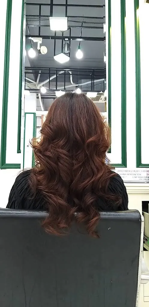 Long copper-brown curls seen from behind in a styling chair, a perm finished at Nien Is New hair salon in Da Nang