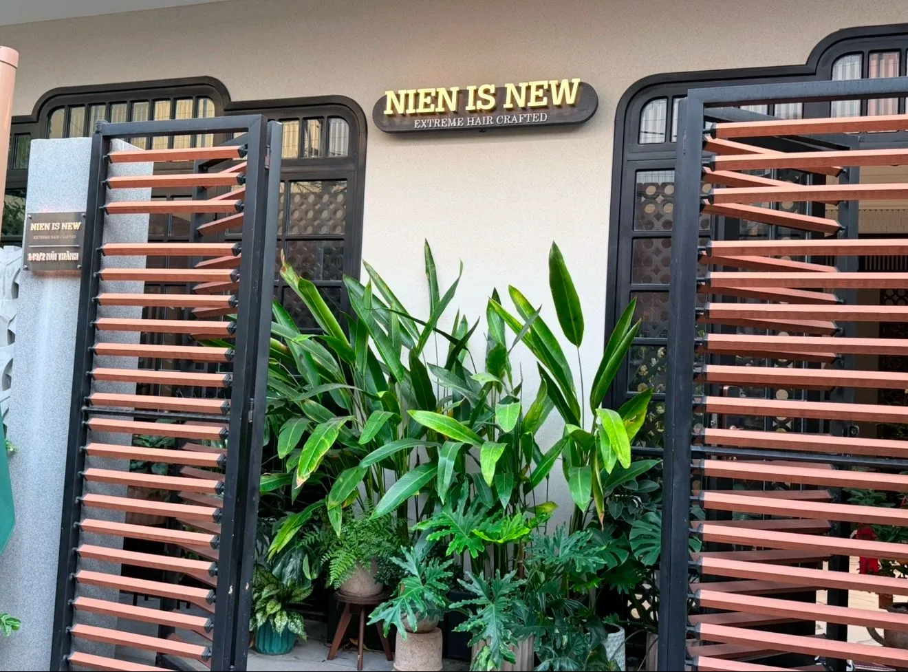 Storefront of Nien Is New hair salon on Núi Thành street, Da Nang, with wooden louver gates, tropical plants and brass sign